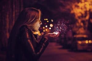 Magical Resolutions created by setting intentions for the New Year denoted by a woman blowing a sparkle in her hand