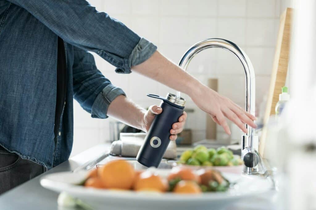 person in blue denim jacket holding stainless steel bottle with hydration drinks