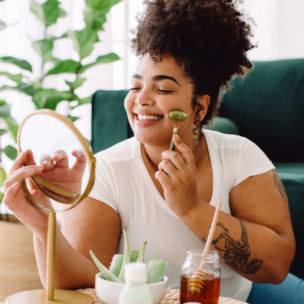 Woman performing self care practices looking in a mirror with beauty products surrounding her symbolizing having a self care plan in place.