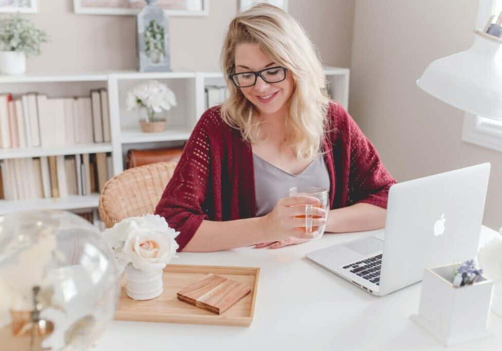 woman smiling holding glass mug sitting beside table with MacBook