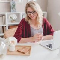 woman smiling holding glass mug sitting beside table used as a mockup for Voxer wellness consultations.